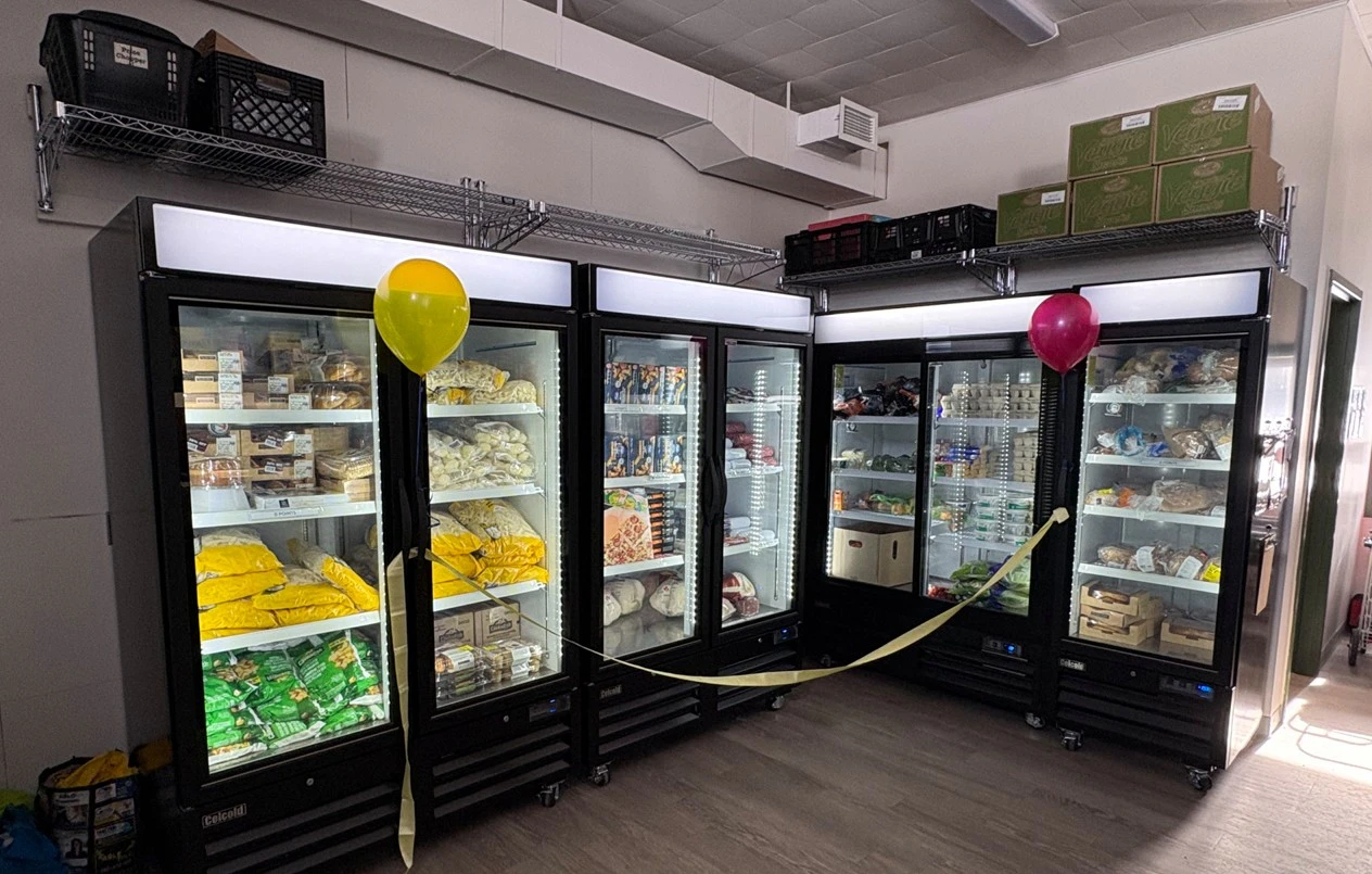 Two glass door fridges and freezers with balloons and streamers decorating them.